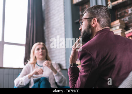 Bearded man feeling thoughtful answering questions of psychologist