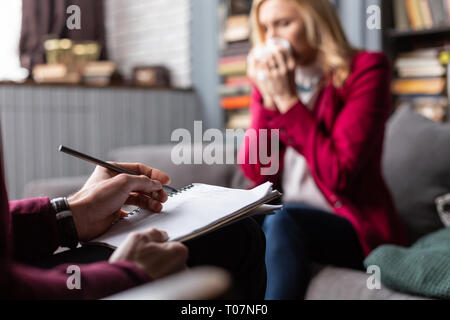 Close up of private therapist making some notes while listening to client Stock Photo