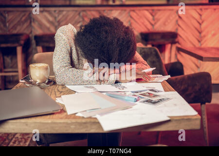 Tired woman sadly leaning on table covered with designer drawings Stock Photo
