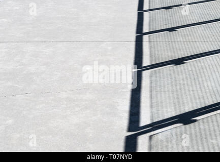 Diagonal shadows and wire mesh pattern on cement walkway from metal and glass panel fence barrier. Stock Photo
