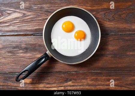 Fried eggs in a frying pan on a wooden background with copy space. Breakfast from natural fresh products. Top view. Stock Photo