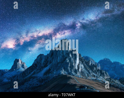 Milky Way above mountains at night in summer. Landscape with alpine mountain valley, blue sky with milky way and stars, buildings on the hill, rocks.  Stock Photo