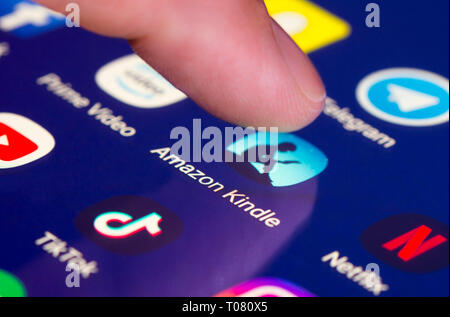 Finger pressing Amazon Kindle app icon on a touchscreen on a tablet or mobile phone device. Loading Amazon Kindle application. Kindle shortcut. Stock Photo