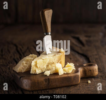 Piece of Parmesan cheese and cheese knife on the wooden board. Dark background. Stock Photo