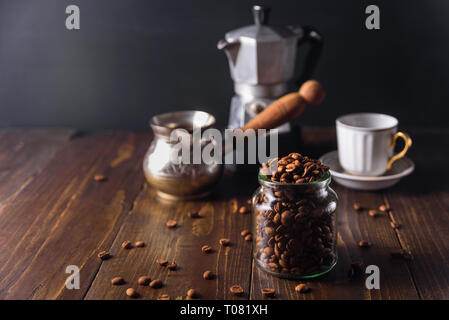 Coffee beans in glass jar on dark wooden background with cezve, geyser coffee maker Stock Photo
