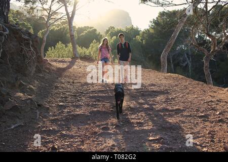 Teenagers hiking with dog running in front in forest Stock Photo