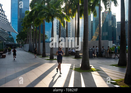 26.12.2018, Singapore, Singapore, Singapore - A jogger walks along the shore of Marina Bay, while in the background the skyscrapers of Singapore's bus Stock Photo