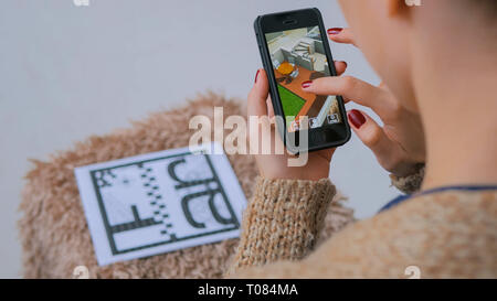 Woman using smartphone with augmented reality app, checking virtual house plan Stock Photo