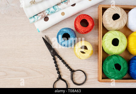 Composition with sewing, knitting threads, fabrics and antique scissors on gray wooden background, top view Stock Photo