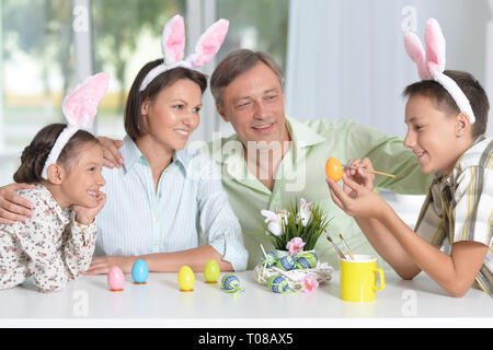 Portrait of family of four wearing bunny ears and painting Easter eggs at home Stock Photo