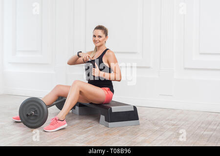Happy beautiful young athletic causcasian woman pink shorts and black top siting, drink water and have a rest after hard working on the gym. Indoor, s Stock Photo