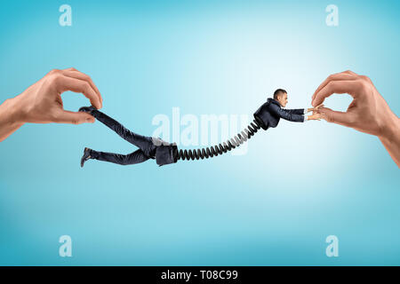 Close-up of two hands holding little businessman split in two parts at waist which are connected with cable wire. Stock Photo
