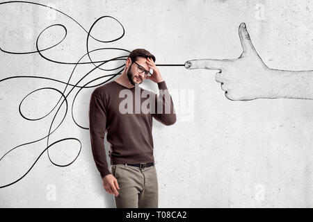 Thinking young man in casual clothes with a hand shooting gesture and abstract lines drawn on white wall background Stock Photo