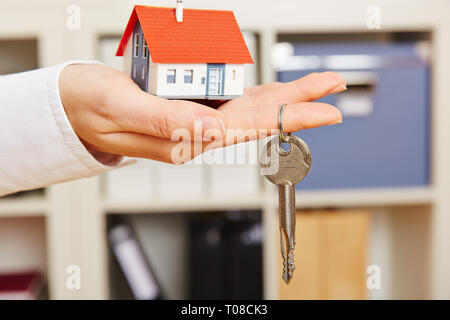 Hand of a woman holds a small house with key Stock Photo
