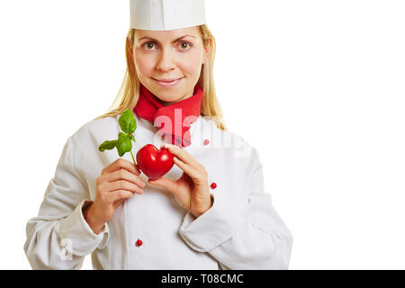 Young cook holds a red heart and green basil Stock Photo