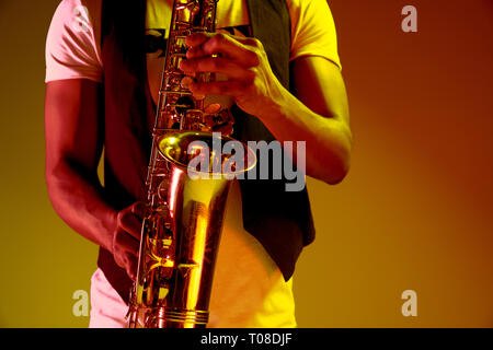 African American handsome jazz musician playing the saxophone in the studio on a neon background. Music concept. Young joyful attractive guy improvising. Close-up retro portrait. Stock Photo