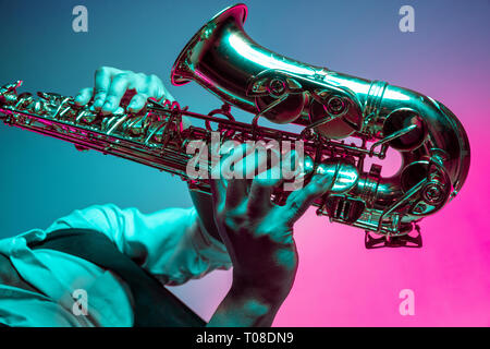 African American handsome jazz musician playing the saxophone in the studio on a neon background. Music concept. Young joyful attractive guy improvising. Close-up retro portrait. Stock Photo