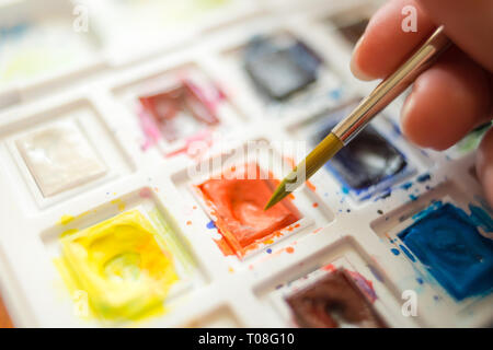 hand holding watercolor brush over a set of watercolor paint closeup. Stock Photo