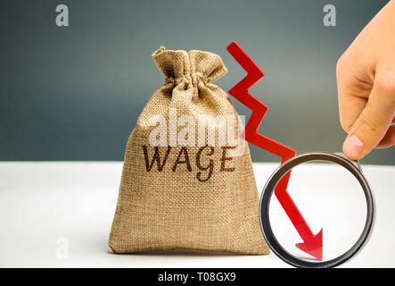 Bag with money and the word Wage and a red down arrow. Salary reduction. Drop in profits. Financial crisis. Demotion. Low profit. Capital outflow. Con Stock Photo