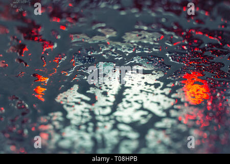 Car running through automatic carwash. Windscreen view from inside. Abstract wet windshield background. Red brake lights of car ahead. Washing conveyo Stock Photo