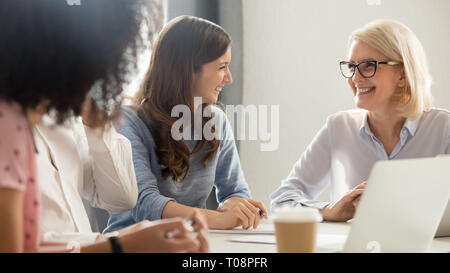 Friendly smiling old and young businesswomen talking laughing at meeting Stock Photo