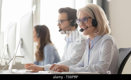 Smiling old female call center agent in headset consulting client Stock Photo