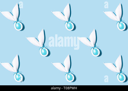 Pattern made of Easter bunny ears made of white napkin with egg on blue background. Minimal styled easter card concept.