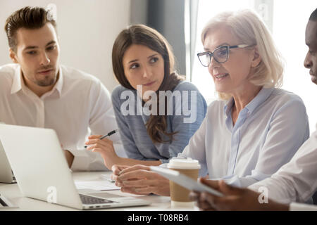 Focused young interns making notes listening to old female manager Stock Photo