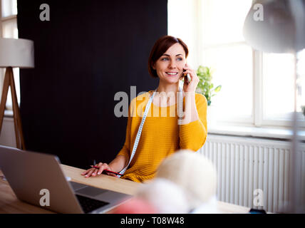Young creative woman in a studio, using smartphone. A startup of tailoring business. Stock Photo