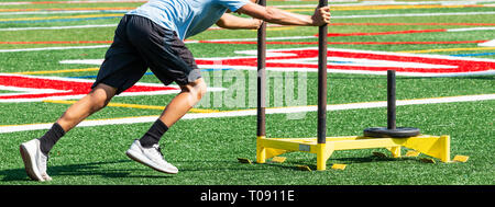 A high school cross country runner is pushing a yellow sled with weight on it during preseason strength and agility practice. Stock Photo