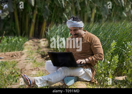 Happy farmer or village man operating a laptop computer in his agriculture field. Stock Photo