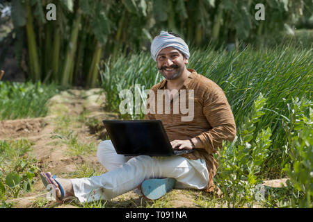 Happy farmer or village man operating a laptop computer in his agriculture field. Stock Photo