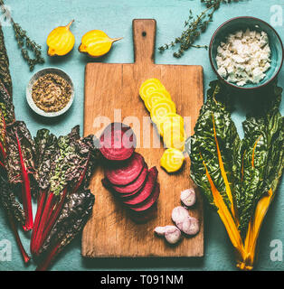 Colorful sliced beetroots with greens ingredients on kitchen table with cutting board, top view. Healthy vegetarian eating and cooking Stock Photo