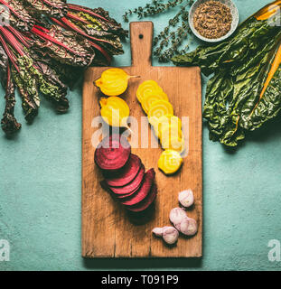 Colorful sliced beetroots with greens ingredients on kitchen table with cutting board, top view. Healthy vegetarian eating and cooking Stock Photo