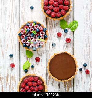 Raspberry and blueberry tartlets with chocolate ganache, fresh berries and mint leaves, selective focus. Fresh fruit tart on white background, freshly Stock Photo