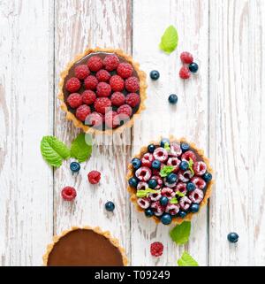 Raspberry and blueberry tartlets with chocolate ganache, fresh berries and mint leaves, selective focus. Fresh fruit tart on white background, freshly Stock Photo