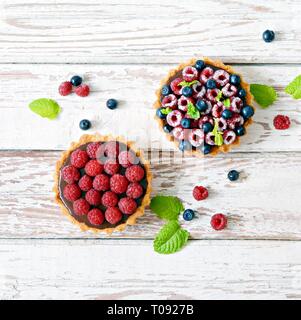 Raspberry and blueberry tartlets with chocolate ganache, fresh berries and mint leaves, selective focus. Fresh fruit tart on white background, freshly Stock Photo