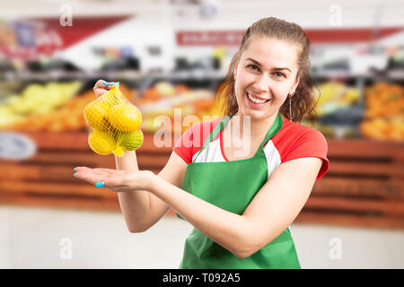 Smiling female grocery store or supermarket employee presenting bag of lemons with hands and trustworthy expression Stock Photo