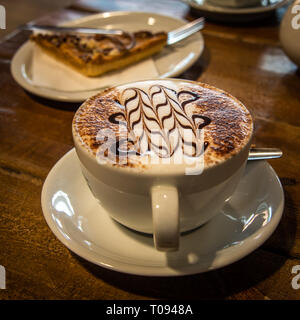 A hot cup of cappuccino coffee and a cake on a wooden table Stock Photo