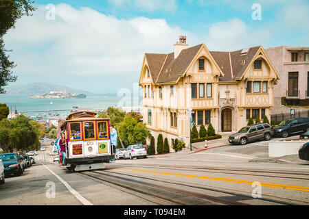 Powell-Hyde cable car climbing up steep hill in central San Francisco with famous Alcatraz Island in the background on a sunny day with blue sky, USA Stock Photo