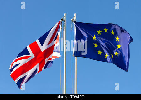 United Kingdom flag vs. European Union flag on flagpole in front of blue sky