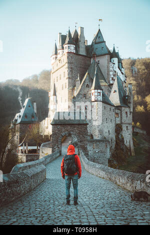 Panorama view of young explorer with backpack taking in the view at famous Eltz Castle at sunrise in fall, Rheinland-Pfalz, Germany
