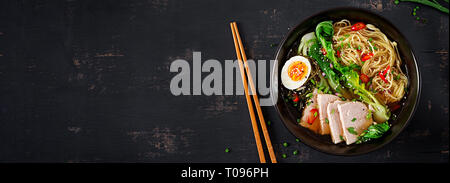 Miso Ramen Asian noodles with egg, pork and pak choi cabbage in bowl on dark background. Japanese cuisine. Top view. Banner Stock Photo