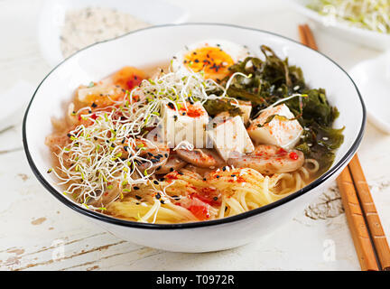 Miso Ramen Asian noodles with cabbage kimchi, seaweed, egg, mushrooms and cheese tofu in bowl on white wooden table. Korean cuisine. Stock Photo