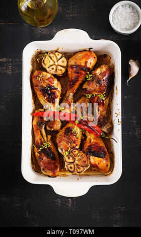 Appetizing oven baked golden chicken drumsticks  in a baking dish on a dark table. Asian cuisine. Top view Stock Photo