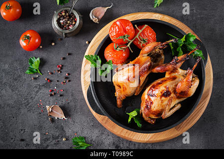 Baked quails in pan on a dark background. Top view. Free space for your text. Stock Photo