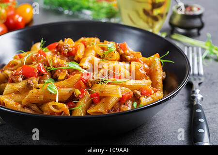Penne pasta in tomato sauce with meat, tomatoes decorated with pea sprouts on a dark table. Stock Photo