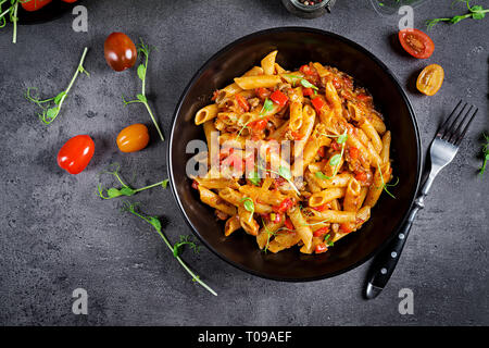 Penne pasta in tomato sauce with meat, tomatoes decorated with pea sprouts on a dark table. Top view