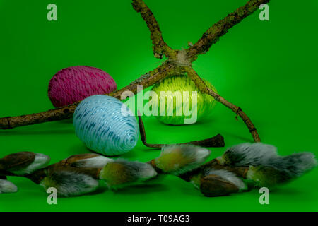 Handmade Easter eggs, soft willow buds and cross of twigs in close-up on green background. Christian symbols of Palm Sunday or Easter Stock Photo