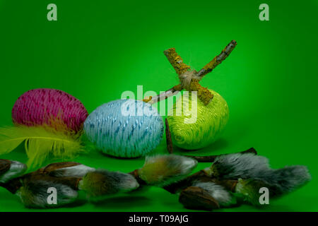 Handmade Easter eggs, soft willow buds and cross of twigs in close-up on green background. Christian symbols of Palm Sunday or Easter Stock Photo